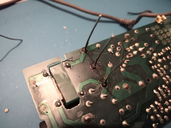 Underside of a Mac PowerBook power supply circuit board, showing tracks and solder pads/blobs. Three unsnipped legs (of a RIFA capacitor) are poking through the holes, with fresh solder.