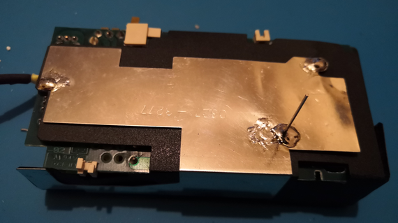 Underside of a Mac PowerBook power supply circuit board, showing the freshly-soldered ground plate on top of the black card insulating it from the main circuit board.