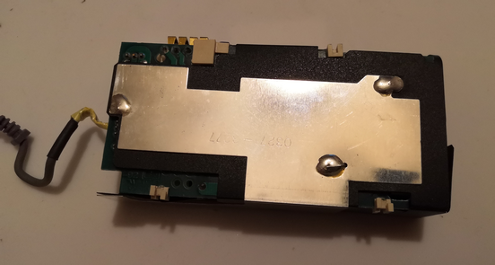 Inside of a Mac PowerBook Duo power supply, showing the underside of the main circuit board, which is covered by black card and a soldered-on metal ground plate.